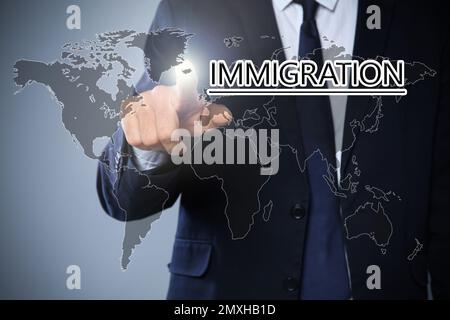 Uomo d'affari che tocca l'IMMIGRAZIONE di parola sullo schermo virtuale contro lo sfondo grigio, primo piano Foto Stock