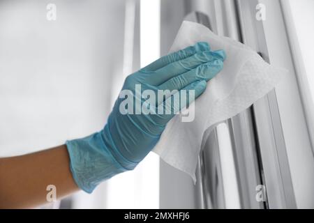 Donna che pulisce la maniglia della porta con la salvietta bagnata per interni, primo piano Foto Stock