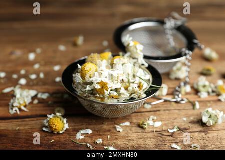 Fiori di camomilla asciutti in infusore su tavolo di legno, primo piano Foto Stock