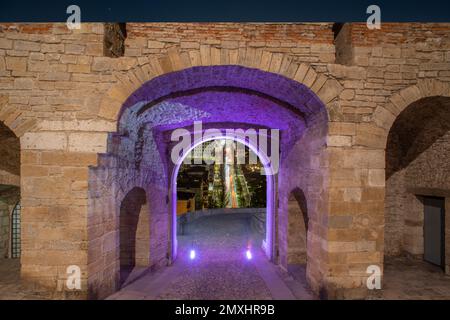 Porta San Giacomo illuminata con lo sfondo della città di Bergamo Foto Stock