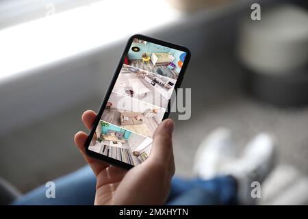 Uomo che controlla le telecamere CCTV moderne sullo smartphone in interni, primo piano. Sistema di sicurezza domestica Foto Stock