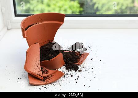 Vaso di terracotta rotto con terreno su davanzale bianco al coperto Foto Stock