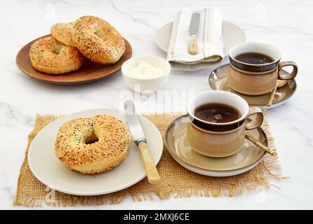 Bagel freschi e formaggio cremoso con tazze e piattini per la pausa caffè in formato orizzontale e shot in luce naturale. Foto Stock