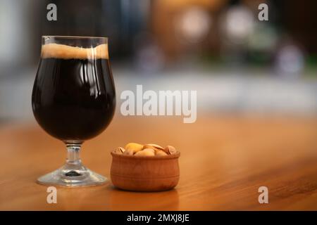 Bicchiere di birra fredda e gustosa e scura servita con arachidi su un tavolo di legno Foto Stock