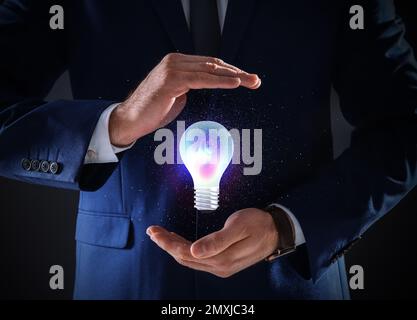 Concetto di idea. Uomo d'affari che mostra la lampadina luminosa illustrazione su sfondo scuro, primo piano Foto Stock