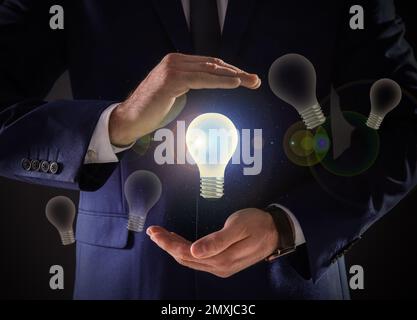 Concetto di idea. Uomo d'affari che mostra una lampadina luminosa su sfondo scuro, primo piano Foto Stock