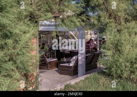 terrazza esterna, circondata da cespugli e alberi verdi, per un bar, caffetteria, ristorante, con divani, Tavoli e persone sedute, sulla Virgen del Mar Foto Stock