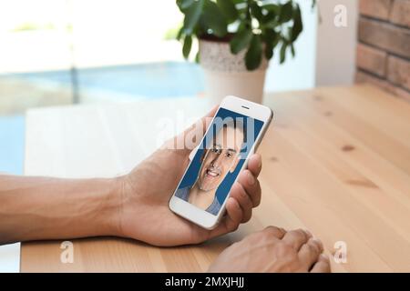 Uomo che utilizza lo smartphone con sistema di riconoscimento facciale al tavolo al chiuso, primo piano. Verifica biometrica Foto Stock