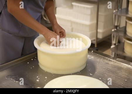 Lavoratore che prende formaggio fresco dalla muffa in fabbrica moderna, primo piano Foto Stock