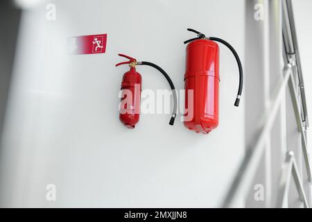 Estintori e segnale di uscita di emergenza su una parete bianca all'interno Foto Stock