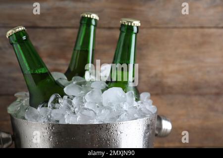 Secchio in metallo con birra e cubetti di ghiaccio su fondo in legno, primo piano Foto Stock
