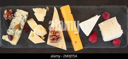 Diversi tipi di deliziosi formaggi e snack su piatto di ardesia, piatto Foto Stock