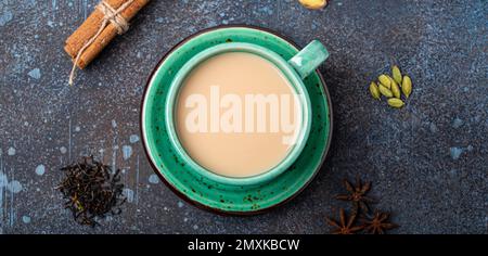 Sana bevanda indiana masala chai - tè bevanda calda con latte e spezie in rustico verde teacup con ingredienti per la preparazione di masala chai dall'alto in su Foto Stock