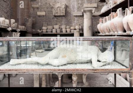 Archeologia, calco in gesso di un uomo reclinabile in vetrocamera di fronte alle anfore, antica città romana di Pompei, Pompei, nei pressi di Napoli, Campania, Italia Foto Stock