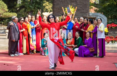 Una donna gesta come un grande gruppo di donne per lo più vietnamite vestite di colorato tradizionale ao dai, organizzarsi per posare per una foto di gruppo dentro Foto Stock