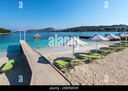 Ksamil, Albania - 15 settembre 2021: Ombrelloni in file sulla spiaggia di sabbia vuota Ksamil Ucraina con passaggio pedonale in legno con doccia in Albania Foto Stock