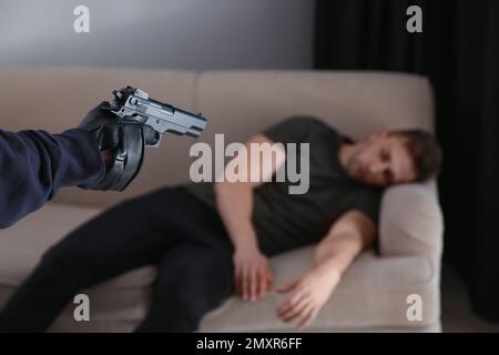 Uomo con la pistola e la vittima in camera, primo piano. Criminale pericoloso Foto Stock