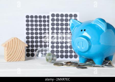 Composizione con pannelli solari e banco di porcellini su tavolo di legno bianco Foto Stock