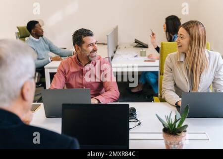 Un bell'uomo d'affari senior sta ascoltando la sua collega bionda femminile raccontando una storia divertente. Stanno ridendo Foto Stock