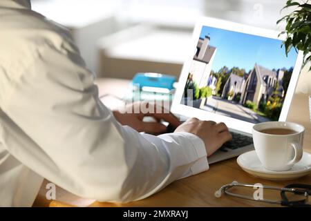 Servizio online agenzia immobiliare. Medico scegliendo nuova casa via laptop, primo piano Foto Stock