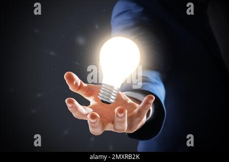 Concetto di idea. Uomo d'affari che mostra la lampadina luminosa illustrazione su sfondo scuro, primo piano Foto Stock