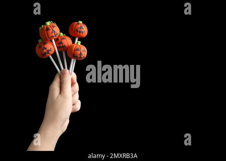 Donna con deliziosi pop di torta a forma di zucca e spazio per il testo su sfondo nero, primo piano. Festa di Halloween Foto Stock