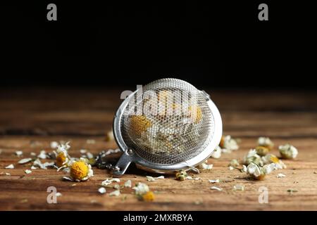 Fiori di camomilla asciutti in infusore su tavolo di legno, primo piano Foto Stock