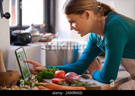 Scegliere una ricetta online. una giovane donna che guarda una ricetta online sul suo tablet digitale. Foto Stock