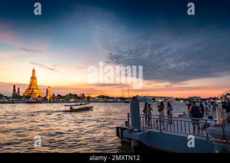 Al crepuscolo, la silhouette di una barca da diporto che passa davanti alle pagode dorate del complesso del tempio, mentre le persone si riuniscono in un punto di vista sul lato opposto Foto Stock