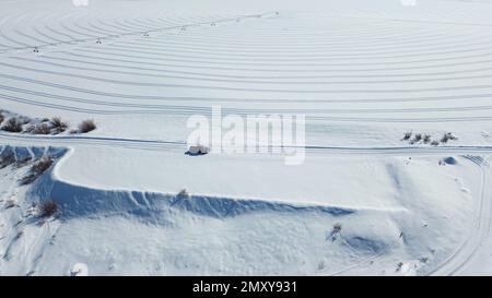Un colpo aereo su un campo coperto di neve e un pickup car che guida sulla strada innevata Foto Stock