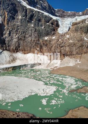 Uno scatto verticale di un piccolo lago ghiacciato sulla cima della montagna rocciosa in una giornata di sole Foto Stock