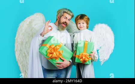 Piccolo angelo bambino con dono e uomo bearded in ali angeliche mostra segno ok. Shopping di San Valentino. Foto Stock