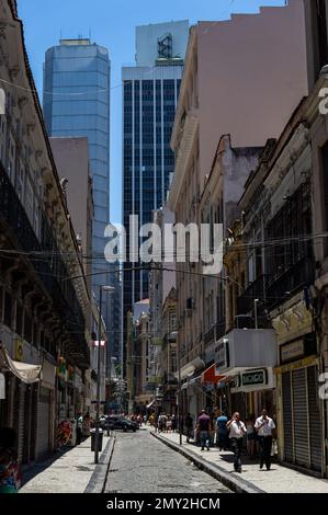 Vista della stretta strada acciottolata Miguel Couto nel quartiere Centro circondato da alti edifici commerciali sotto il cielo limpido del pomeriggio estivo. Foto Stock