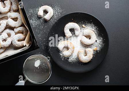 Cottura biscotti tradizionali alla vaniglia e in polvere con zucchero di ricino. Concetto di cottura di festa su sfondo nero Foto Stock