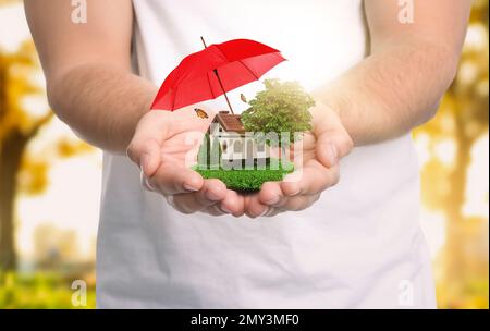 Concetto assicurativo - ombrello dimostrante protezione. Uomo in casa modello con prato verde, primo piano Foto Stock