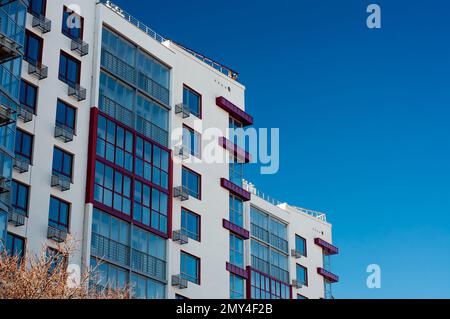 Frammento della facciata di un moderno edificio di appartamenti, pareti bianche e balconi di vetro contro il cielo blu Foto Stock