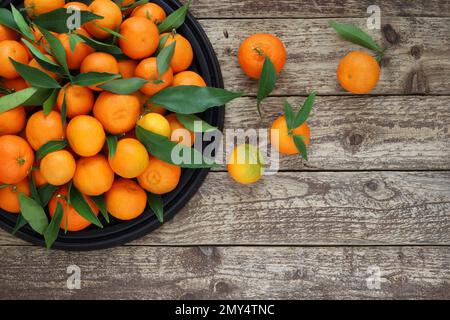 Arance mandarine con foglie su vassoio nero su sfondo di legno, vista sul tavolo superiore. Sfondo di frutta fresca di mandarini su tavola di legno con spazio copia. Foto Stock