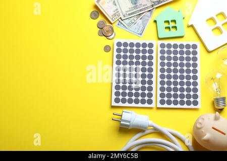 Composizione a posa piatta con pannelli solari e banco di porcellini su sfondo giallo. Spazio per il testo Foto Stock