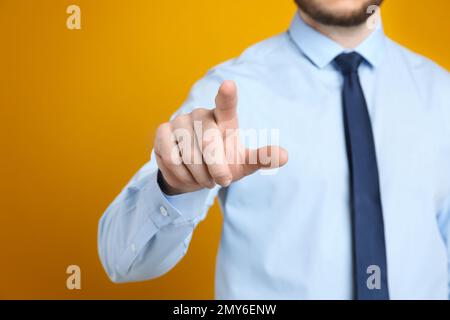 Uomo d'affari che tocca qualcosa contro lo sfondo arancione, fuoco a portata di mano Foto Stock