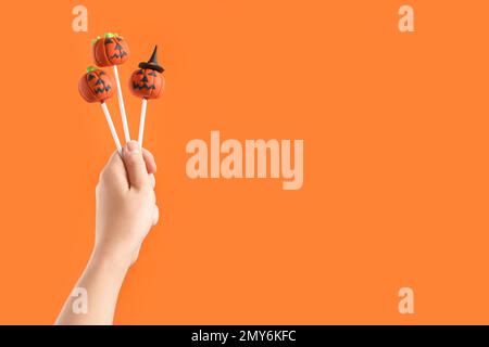 Donna con deliziosi pop di torta a forma di zucca e spazio per il testo su sfondo arancione, primo piano. Festa di Halloween Foto Stock