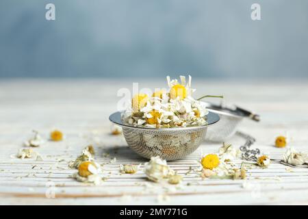 Fiori di camomilla asciutti in infusore su tavolo di legno bianco, primo piano Foto Stock