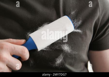 Uomo che rimuove i capelli dalla maglietta grigia con un rullo per pelucchi, primo piano Foto Stock