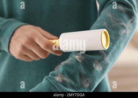 Uomo che rimuove i capelli dalla felpa verde con rullo per pelucchi su sfondo chiaro, primo piano Foto Stock