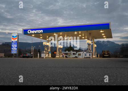 Sultan, WA, USA - 1 febbraio 2023; distributore di benzina Chevron illuminato di fronte alle montagne in WA Foto Stock