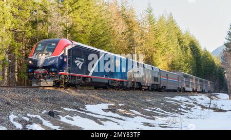 Skykomish, WA, USA - 1 febbraio 2023; treno con cuccetta Amtrak Empire Builder in inverno con ghiaccio sull'unità principale passando per le Montagne Cascade di Washington Foto Stock