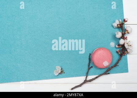 Amaretti rosa e un ramo con i fiori di albicocca. Fondo turchese vuoto su tavole di legno bianche. Modello per la progettazione. Layout piatto, superiore Foto Stock