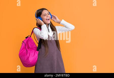 il bambino stupito in cuffie con zaino scuola su sfondo giallo. Foto Stock