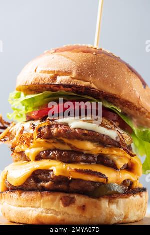 Cheeseburgers caricato tre polpette triplicate impilate alte con strati di formaggio, lattuga e pomodoro. Cheeseburger alto Foto Stock