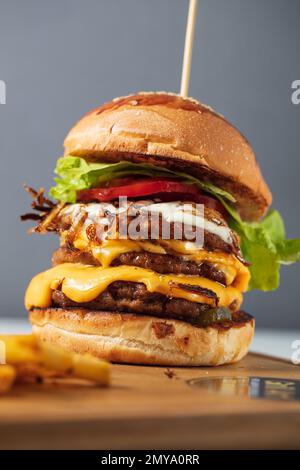 Cheeseburgers caricato tre polpette triplicate impilate alte con strati di formaggio, lattuga e pomodoro. Cheeseburger alto Foto Stock