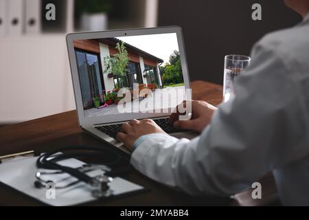 Servizio online agenzia immobiliare. Medico scegliendo nuova casa via laptop, primo piano Foto Stock